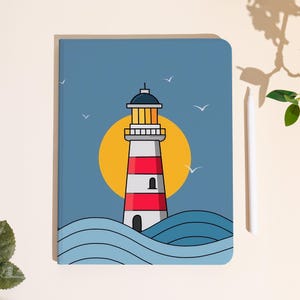 Könnte beinhalten: Ein blaues Notizbuch mit einer Leuchtturm-Illustration. Der Leuchtturm hat rot-weiße Streifen, einen schwarzen Deckel und ist vor einer gelben Sonne und blauen Wellen platziert. Weiße Möwen fliegen am Himmel. Ein weißer Stift befindet sich rechts.