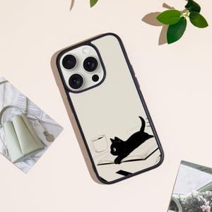 May include: A phone case with a black and white illustration of a black cat on a desk with a coffee cup. The case has a cream-colored background and a black border.