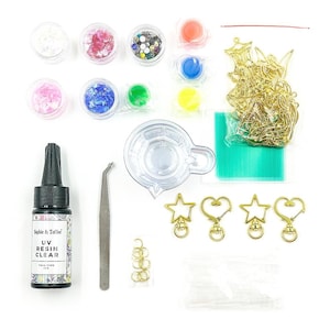 Puede incluir: Un kit de manualidades con varios suministros para arte en resina. Incluye resina UV, purpurina, abalorios dorados, vasos mezcladores y pinzas. El kit presenta una variedad de colores y texturas, perfecto para crear joyas y objetos decorativos únicos.