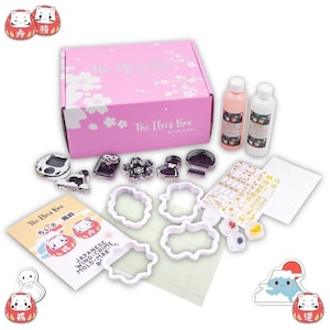 Puede incluir: Una caja rosa con el texto "The Elves Box" en la parte delantera. La caja contiene una variedad de artículos, incluyendo cortadores de galletas, pegatinas y botellas de pintura. Los artículos están todos relacionados con las campanas de viento japonesas. El texto "ちいさ 風鈴" está en una tarjeta blanca.