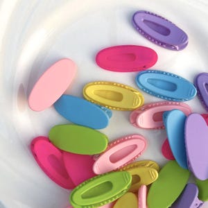 Puede incluir: Una colección de coloridas pinzas para el pelo ovaladas en varios tonos de rosa, morado, amarillo, azul y verde. Las pinzas son de plástico y tienen un diseño sencillo y funcional. Medidas no disponibles.
