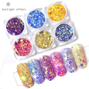 May include: A collection of colorful nail art glitter in small, clear square containers. The glitter comes in various colors, including gold, blue, purple, pink, and yellow. The image also shows several manicured nails with glitter applied, showcasing the different color options. The text "Sunlight effect" is visible.