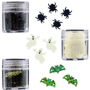 Puede incluir: Suministros de manualidades con temática de Halloween que incluyen purpurina negra, formas de fantasmas blancos, murciélagos con purpurina verde y dorada y pequeños frascos con elementos decorativos.