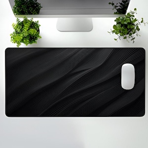 May include: Black desk mat with a wavy, textured design. A white computer mouse is on the mat.