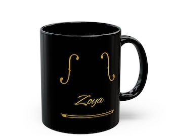 May include: Black ceramic mug with a gold violin design. The design includes two f-holes, the name "Zoya", and a violin bow. The mug has a curved handle and a glossy finish.