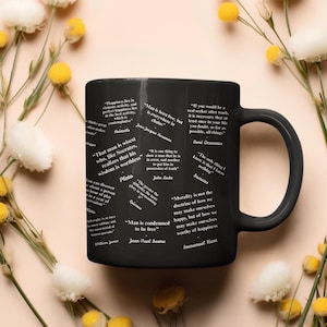 Puede incluir: Taza de cerámica negra con citas de filósofos como Platón y Sócrates en blanco. La taza tiene un asa negra y está rodeada de flores.