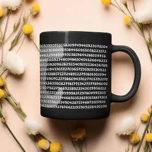 May include: A black ceramic coffee mug with a white numerical pattern printed on the side. The mug has a curved handle and is surrounded by yellow flowers.