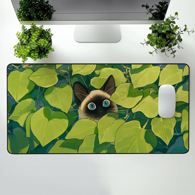 Puede incluir: Alfombrilla de rat&oacute;n rectangular con un gato siam&eacute;s mirando a trav&eacute;s de hojas verdes. El gato tiene ojos azules y una cara marr&oacute;n con orejas marrones oscuras. Un rat&oacute;n de ordenador blanco est&aacute; a la derecha. El fondo es azul claro.