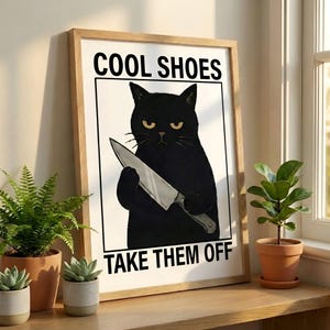 Può includere: Stampa artistica incorniciata con un'illustrazione di un gatto nero che tiene un coltello. Il testo recita "COOL SHOES TAKE THEM OFF". Il gatto ha occhi gialli e un'espressione seria. La stampa è in una cornice di legno.