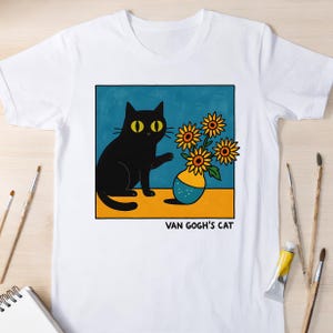 Könnte beinhalten: Weißes T-Shirt mit einer Cartoon-Illustration einer schwarzen Katze mit gelben Augen, die nach Sonnenblumen in einer Vase greift. Das Design ist vor blauem Hintergrund mit dem Text "VAN GOGH'S CAT".