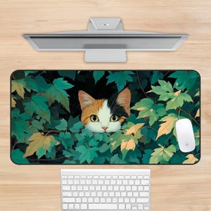 May include: A rectangular mousepad featuring a calico cat peeking through green leaves. The cat has orange, black, and white fur. A white mouse and keyboard are visible below the mousepad. The background is a light wood color.