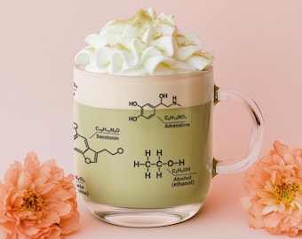 May include: A clear glass mug with a handle, filled with a green beverage topped with whipped cream and a sprinkle of green powder. The mug has a chemical formula printed on it, including the words "Serotonin", "Adrenaline", and "Alcohol (ethanol)".
