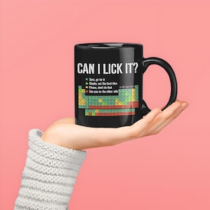 May include: Black ceramic mug with the text "CAN I LICK IT?" in white. The mug features a periodic table of elements design with the phrases "Sure, go for it", "Maybe, not the best idea", "Please, don't do that", and "See you on the other side".
