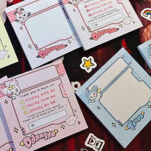 Può includere: Una collezione di blocchi per appunti quadrati in vari colori pastello, tra cui blu, rosa e giallo. Ogni blocco per appunti presenta un personaggio dei cartoni animati, elementi decorativi e il testo "Thank you so much for trading with me".
