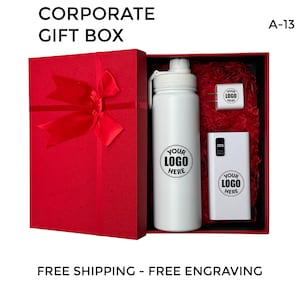 以下が含まれることがあります： 赤いギフトボックスには、白いウォーターボトル、白いモバイルバッテリー、白い壁掛け充電器が入っています。ボックスには赤いリボンと弓が付いています。アイテムはすべて白で、「YOUR LOGO HERE」という文字が印刷されています。
