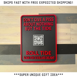 May include: A rectangular sign with a red border and text. The sign reads "DON'T GIVE A PISS ABOUT NOTHING BUT THE TIDE" in red, with a QR code and "ROLL TIDE SCAN FOR DIXIELAND DELIGHT" in red. The background is black.