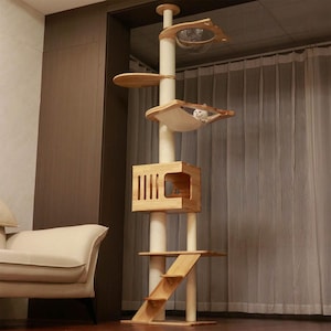 May include: A tall wooden cat tree with multiple levels, including a hammock, a house, and a scratching post. The cat tree is made of natural wood and has a light brown finish. A white cat is resting in the hammock.