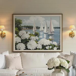 Peut inclure: Salon côtier avec un canapé blanc, des coussins et une table basse en osier. Un tableau encadré de voiliers et de fleurs blanches est accroché au-dessus du canapé. Un vase de fleurs blanches et un plaid bleu complètent le décor.