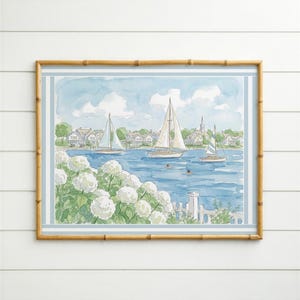 Puede incluir: Una pintura de acuarela en un marco de bambú que representa una escena costera con veleros blancos sobre agua azul, una costa con casas y un primer plano de flores de hortensia blancas. La obra tiene un borde azul claro y un marco de madera.