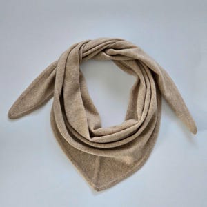 Puede incluir: Una bufanda triangular de color marrón claro hecha de tejido de punto suave.