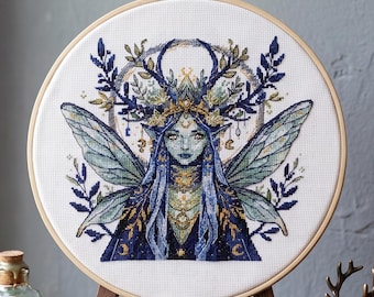 May include: A cross-stitch embroidery of a fairy with blue skin, long blue hair, and delicate wings. The fairy wears a golden crown and ornate jewelry. The design is set in a wooden embroidery hoop, featuring a detailed floral and celestial theme.
