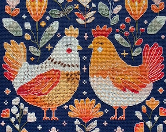 May include: A cross-stitch embroidery on dark blue fabric featuring two chickens facing each other, surrounded by various stylized flowers, leaves, and berries in shades of orange, yellow, white, and green, with small cross-shaped decorative accents.