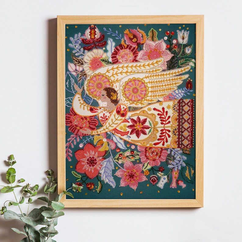 May include: A framed beaded artwork depicting an angel with outstretched wings surrounded by colourful flowers and leaves on a teal background.