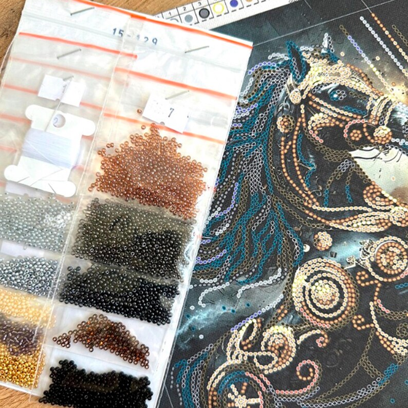 Puede incluir: Un kit de manualidades para un dise&ntilde;o de caballo con cuentas. El kit incluye una imagen parcialmente completada de la cabeza de un caballo con detalles en azul y dorado, junto con peque&ntilde;as bolsas de cuentas de varios colores e hilo blanco. Las bolsas est&aacute;n etiquetadas con n&uacute;meros.