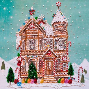 Puede incluir: Ilustración detallada de una casa de jengibre, adornada con glaseado blanco, bastones de caramelo y caramelos de colores. Los árboles de Navidad verdes y las colinas nevadas completan la escena invernal. La obra de arte está adornada con pequeñas cuentas decorativas.
