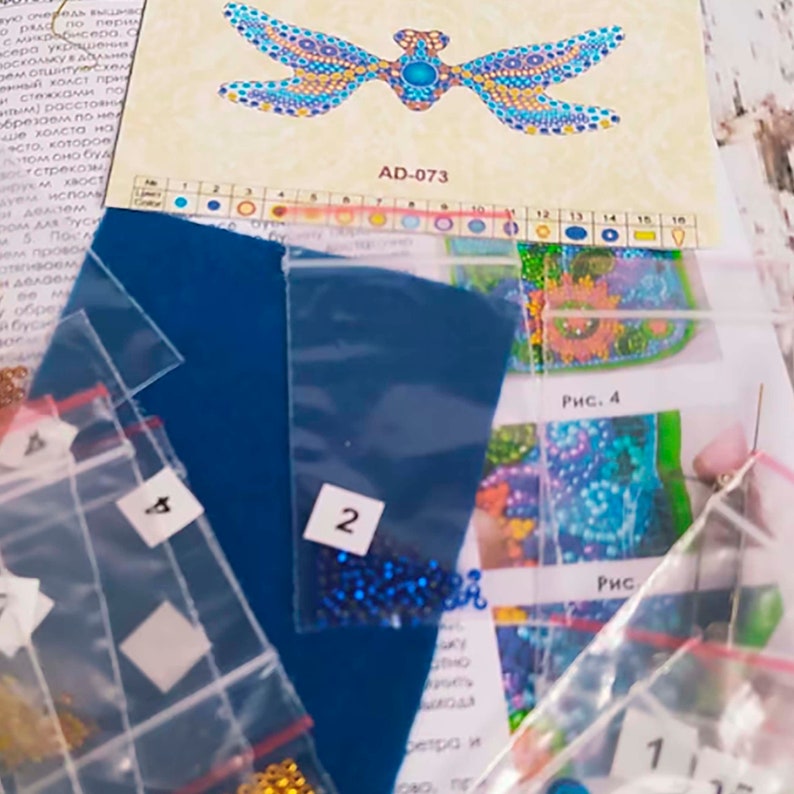 Pode incluir: Um close-up de um kit de pintura de diamantes com um design de lib&eacute;lula. O kit inclui uma tela azul, um saco de contas azuis e uma folha de instru&ccedil;&otilde;es com o design e a tabela de cores. As instru&ccedil;&otilde;es incluem o c&oacute;digo AD-073.
