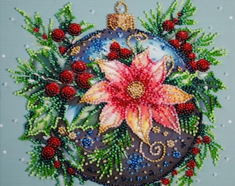 May include: A beaded Christmas ornament with a poinsettia flower and red berries. The ornament is dark blue with gold accents and is surrounded by green pine needles. The background is light blue with white dots.