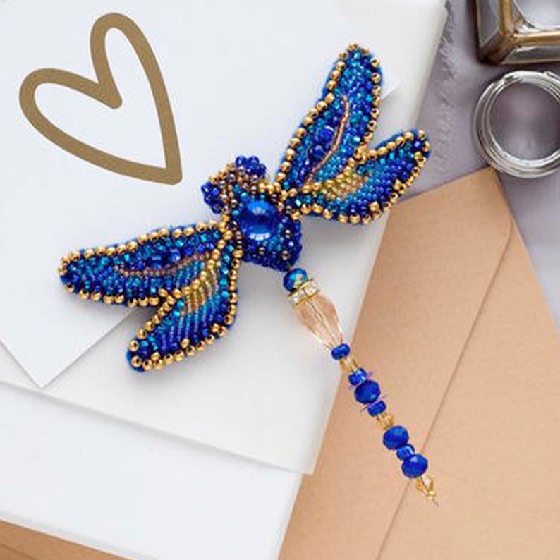 Pode incluir: Um broche de lib&eacute;lula azul e dourado com contas, com um pingente de cristal e contas azuis penduradas na parte inferior.