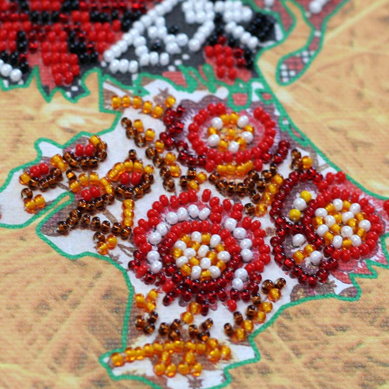 May include: Close-up of a beaded craft project featuring a floral design. The design incorporates red, white, yellow, and brown beads, creating a detailed and textured pattern. The background is a light brown color.