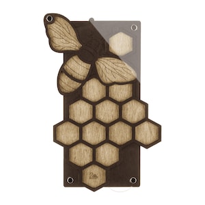 Peut inclure: Une plaque murale rectangulaire en bois avec une base marron foncé et un motif en nid d'abeille en bois clair superposé. Une grande découpe d'abeille en bois détaillée est fixée en haut à gauche. Inclut un revêtement acrylique et des fixations.