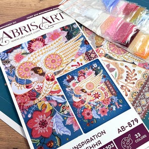 May include: A bead embroidery kit featuring a colourful bird with wings spread, surrounded by flowers. The kit includes 33 colours of beads and the text "Inspiration" and "AB-879".