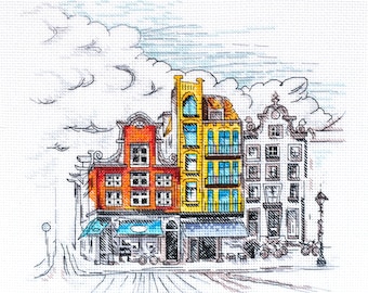 May include: A cross-stitch embroidery pattern depicting a row of three narrow urban buildings. The left building is orange, the center is yellow, and the right is white. The scene includes blue awnings, dark outlines, and stylized clouds above.