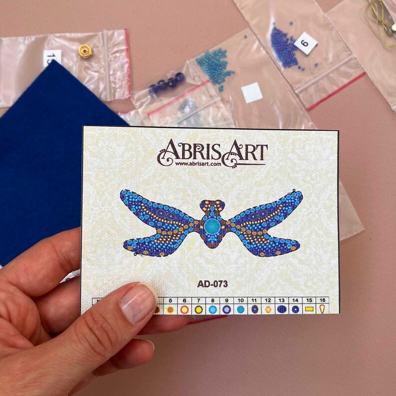 Pode incluir: Um close-up de um kit de mi&ccedil;angas de lib&eacute;lula com um design de lib&eacute;lula azul e dourado. O kit inclui um gr&aacute;fico de cores com 16 cores diferentes de mi&ccedil;angas. O kit &eacute; rotulado como "ABRISART" e "AD-073".