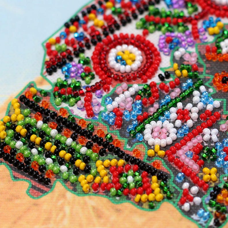 May include: Close-up of a colorful beaded craft project. The design features a circular pattern with red, white, and yellow beads. Other areas are filled with green, black, and blue beads, creating a vibrant and detailed mosaic.
