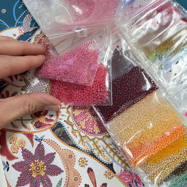 May include: Assortment of small, colourful beads in clear plastic bags. The beads are in various shades of pink, red, orange, and yellow.
