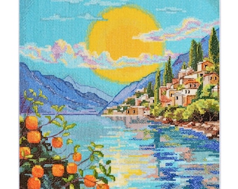 Könnte beinhalten: Ein Kreuzstichmuster, das eine malerische Szene eines kleinen Dorfes zeigt, das an einem ruhigen blauen See liegt. Die Sonne scheint hell am Himmel und wirft einen warmen Schein auf die Berge im Hintergrund. Üppige grüne Bäume und leuchtend orangefarbene Zitrusfrüchte verleihen der Szene einen Hauch von Farbe.