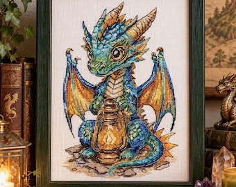 May include: A framed cross-stitch embroidery featuring a small, blue and green dragon with orange-tipped wings holding a glowing yellow lantern. The dragon has large eyes, horns, and a textured scale pattern, set against a white fabric background.