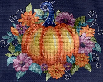 May include: Cross-stitch design featuring a vibrant orange pumpkin with a blue stem, surrounded by colorful flowers in shades of orange, purple, and green. The design is set against a dark blue background.