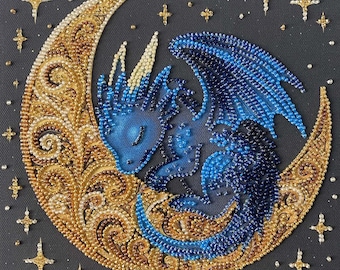 May include: A beaded wall art piece featuring a blue dragon curled within a gold crescent moon. The dragon is crafted from various shades of blue beads, while the moon displays intricate gold and cream swirls. Gold star accents surround the moon.