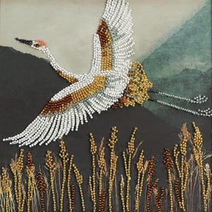 Könnte beinhalten: Ein Perlenkunstwerk, das einen Kranich im Flug darstellt. Der Vogel ist weiß, braun und goldfarben, mit ausgebreiteten Flügeln. Der Hintergrund zeigt eine dunkle Landschaft mit hohen, mit Perlen besetzten Gräsern im Vordergrund.