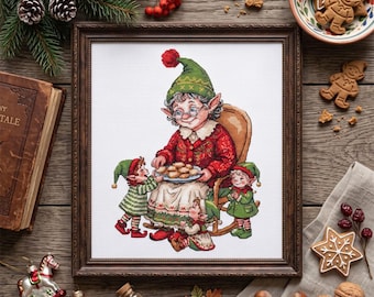May include: A framed cross-stitch embroidery depicting an elderly elf wearing a green hat and red cardigan, seated in a rocking chair while holding a plate of cookies, surrounded by three smaller elves in green clothing, all on a white fabric background.