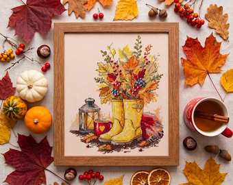 May include: A framed cross-stitch embroidery featuring a pair of yellow rain boots filled with autumn leaves, a lantern, and a mug with a heart. The artwork is surrounded by scattered fall foliage, small pumpkins, berries, and dried orange slices.