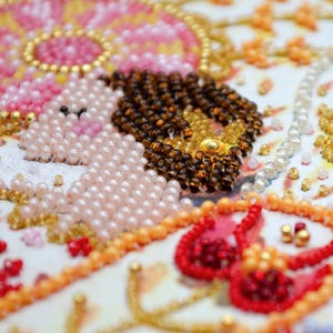 May include: Close-up of a beaded design featuring a pink and white figure with brown hair, surrounded by red, white, and gold beads.