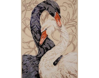 May include: A cross-stitch embroidery piece featuring a black swan and a white swan with orange beaks, their necks curved together to form a heart shape. The background consists of light beige fabric with a faint, outlined floral vine pattern.