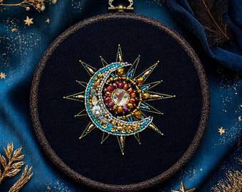 Könnte beinhalten: Ein bestickter Stickrahmen mit einem Mond- und Sonnendesign. Der Mond ist mit türkisfarbenen Perlen, Kristallen und goldenen Akzenten verziert. Die Sonne hat goldene Strahlen und einen zentralen Cluster aus farbigen Edelsteinen. Der Hintergrund ist dunkelblau.