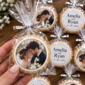 May include: Round sugar cookies with scalloped edges, individually wrapped in clear plastic bags tied with silver ribbons. Each cookie features an edible printed image of a couple or the text Amelia and Ryan with the date 14.09.2024.